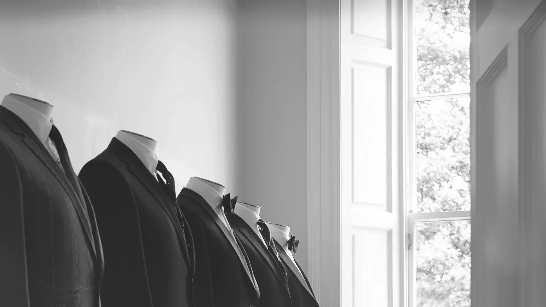 Finished bespoke jackets on tailor's forms by a tall window