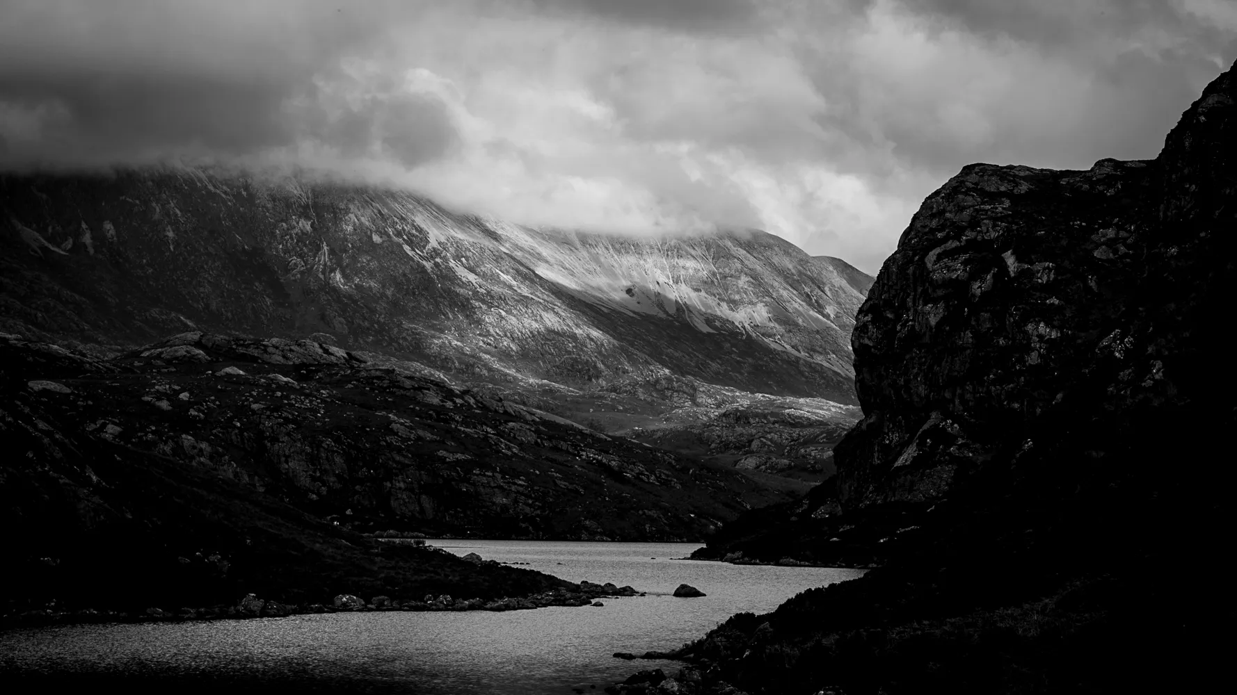 A Highland loch beneath snow-dusted mountains, in black and white