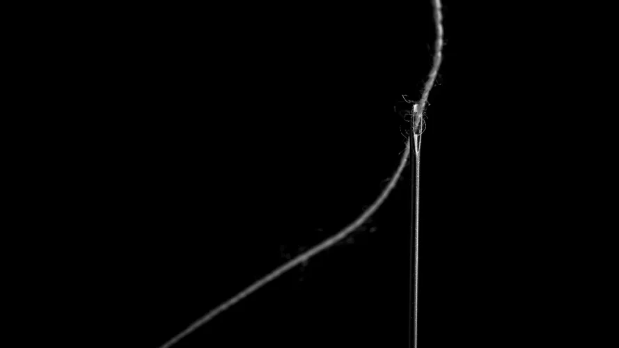 A threaded needle in soft light against black